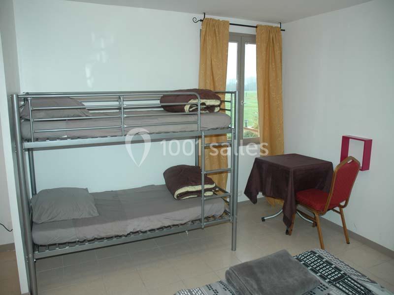 Chambre simple avec lits superposés, table, chaise, fenêtre avec rideaux jaunes et vue sur l'extérieur.