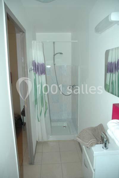 Salle de bain avec une douche à rideau blanc et violet, un lavabo avec serviettes pliées et un miroir mural.