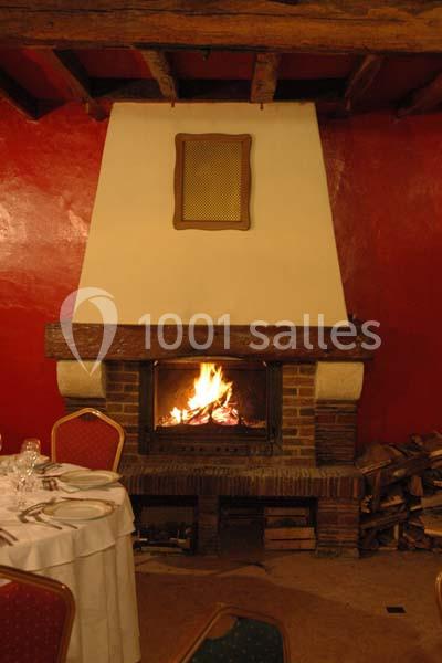 Cheminée en briques avec un feu allumé, entourée de murs rouges et d'une table dressée au premier plan.