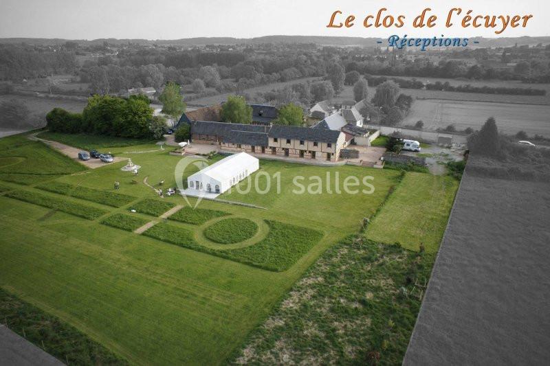 Vue aérienne d'un domaine avec une grande pelouse, une tente blanche et un bâtiment principal entouré de campagne.