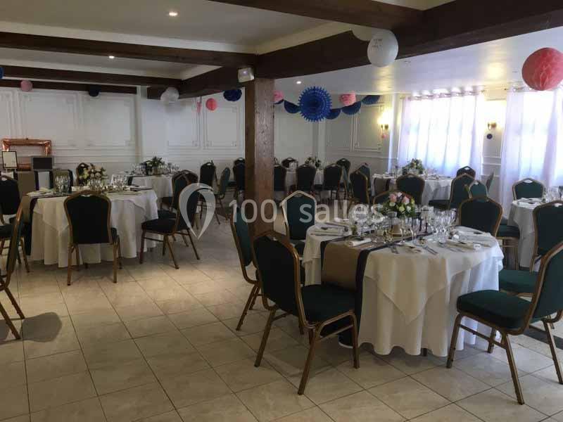 Salle de réception décorée avec des tables rondes dressées, des chaises vertes et des guirlandes suspendues.