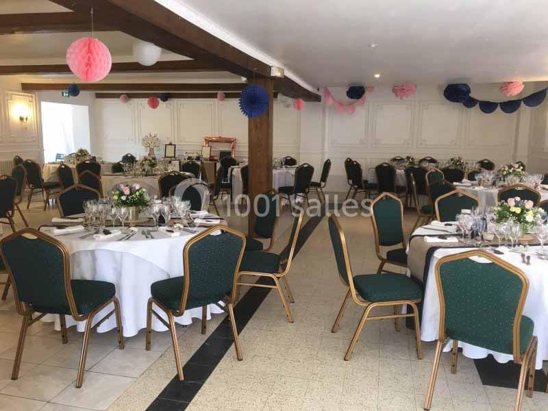 Salle de réception décorée avec des tables rondes dressées, chaises vertes et guirlandes colorées suspendues au plafond.
