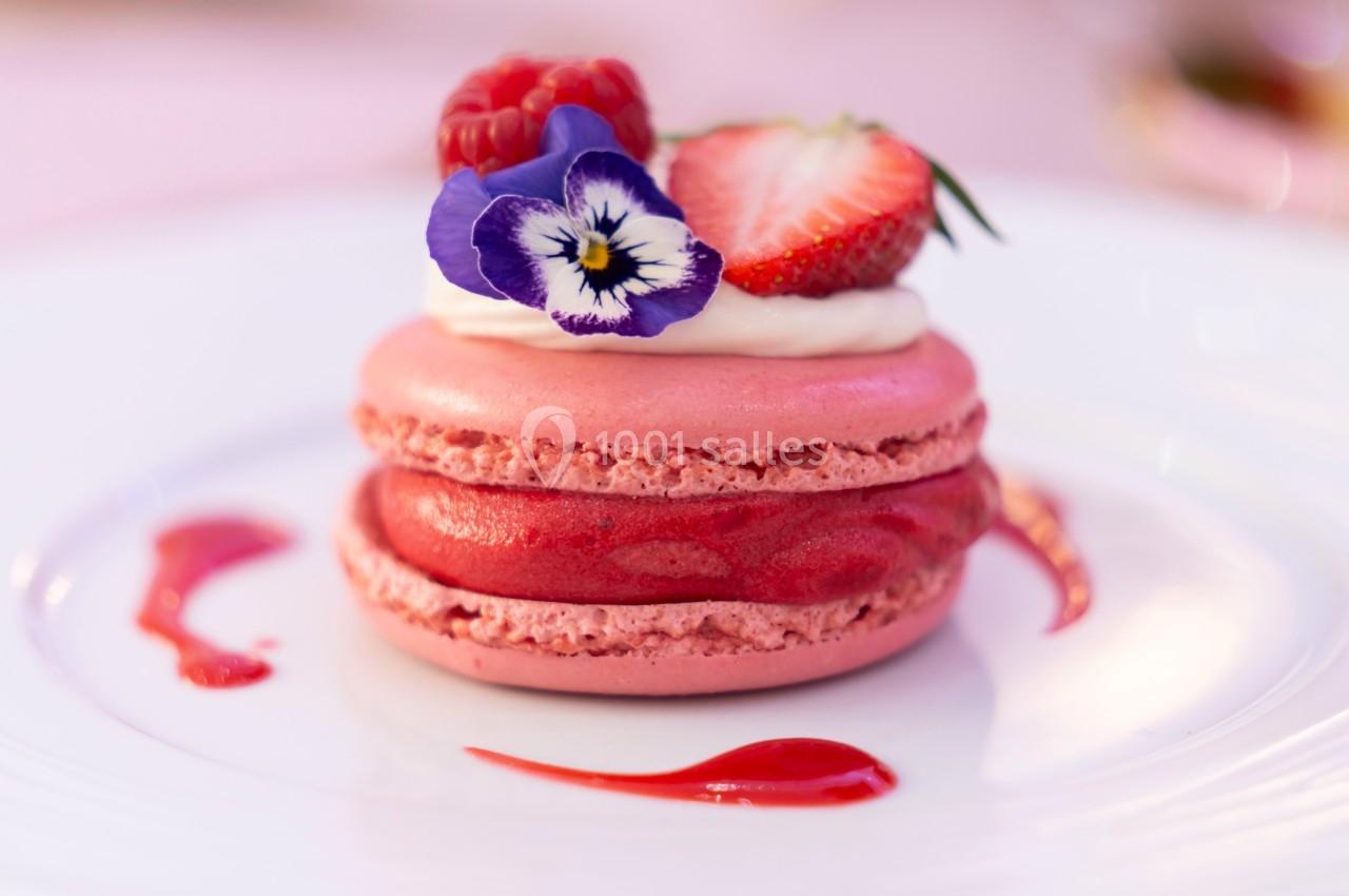 Macaron rose garni de crème, décoré d'une fraise, d'une framboise, d'une fleur comestible et de coulis rouge.