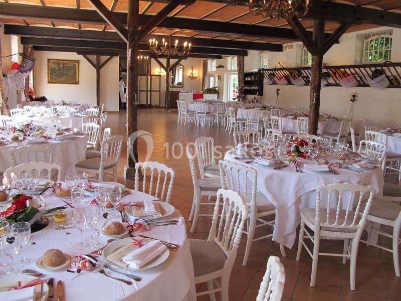 Salle de réception décorée avec des tables rondes dressées, nappes blanches et chaises en bois blanc.