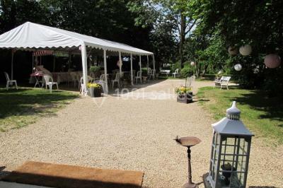 Chaises blanches en plastique disposées sur une pelouse ombragée, avec une tente et un jardin en arrière-plan.