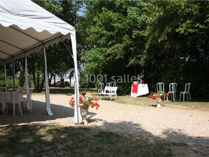 Tente blanche installée en extérieur près d'un chemin gravillonné, avec tables et chaises disposées sous les arbres.