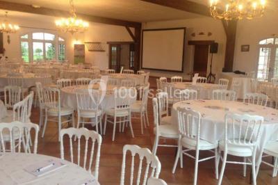 Chaises blanches en plastique disposées sur une pelouse ombragée, avec une tente et un jardin en arrière-plan.