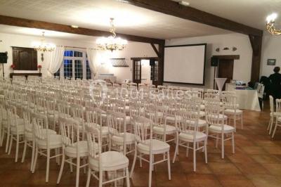 Chaises blanches en plastique disposées sur une pelouse ombragée, avec une tente et un jardin en arrière-plan.