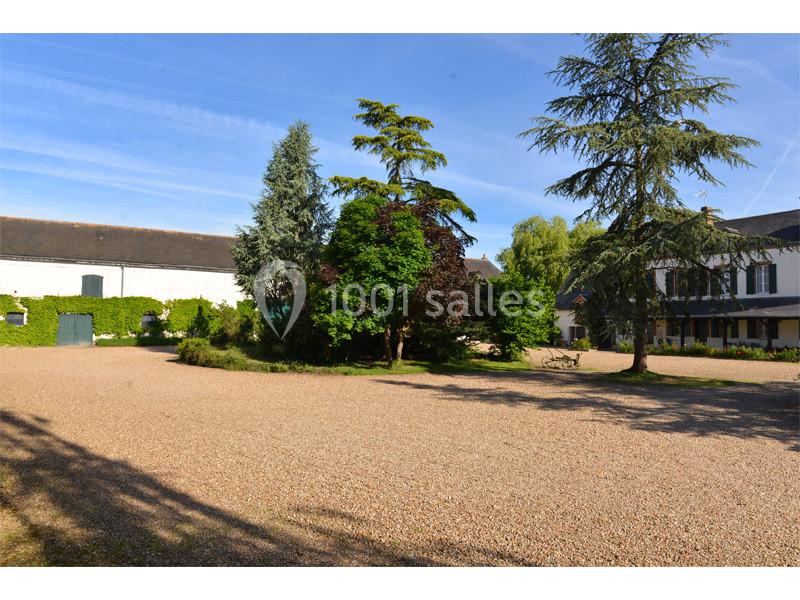 Cour gravillonnée entourée de bâtiments et d'arbres, sous un ciel bleu dégagé.