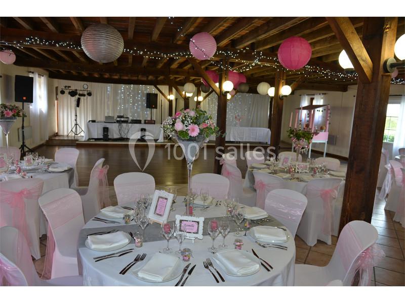 Salle de réception décorée pour un mariage avec tables dressées, chaises blanches ornées de nœuds roses et lanternes…