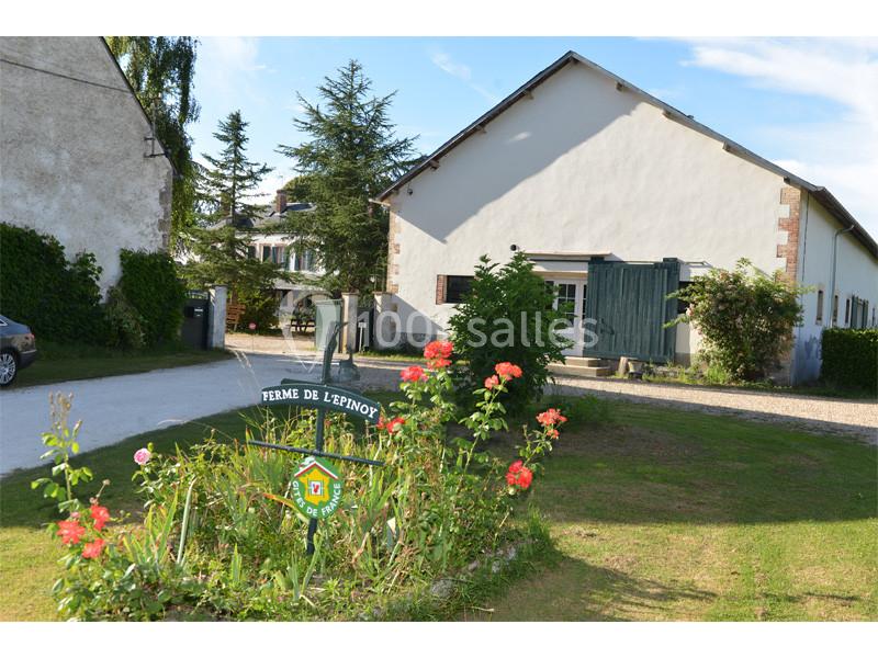 Entrée d'une ferme avec un panneau ’Ferme de l'Erpigny’, entourée de fleurs et de bâtiments ruraux sous un ciel dégagé.