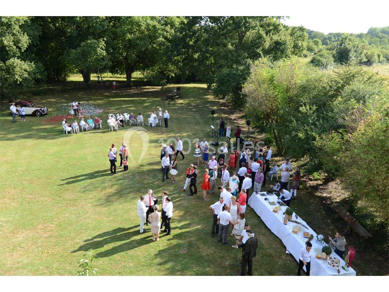 Groupe de personnes rassemblées dans un jardin pour un événement, avec tables dressées et chaises disposées autour.