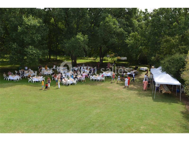 Vue aérienne d'un rassemblement en plein air avec des tables, des chaises et un chapiteau sur une pelouse entourée d'arbres.