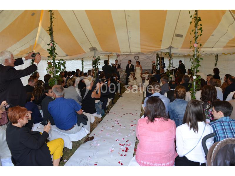 Cérémonie de mariage sous une tente avec des invités assis, un couple devant l'autel et une allée décorée de pétales.