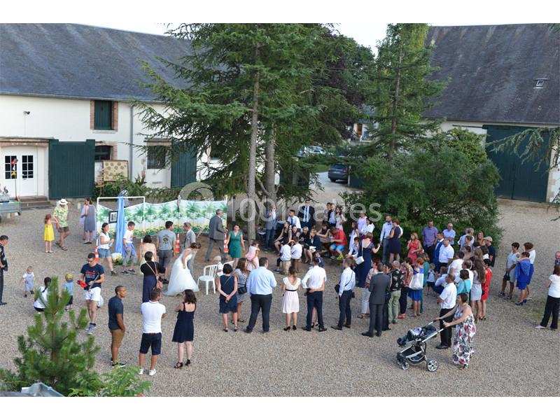 Groupe de personnes rassemblées en extérieur dans une cour gravillonnée, entourée de bâtiments et d'arbres.