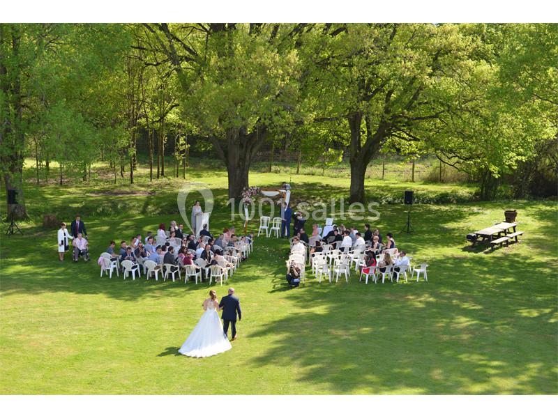 Un mariage en plein air avec des invités assis en cercle sur des chaises blanches, entourés d'arbres verdoyants.