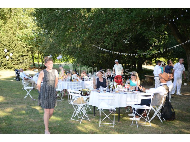 Personnes assises à des tables blanches en extérieur, sous des arbres, lors d'un événement convivial en journée.