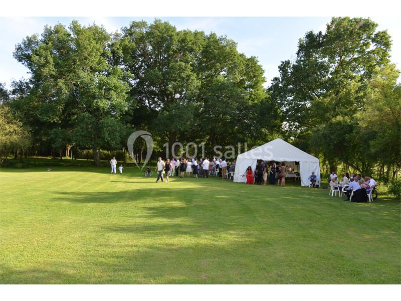 Groupe de personnes rassemblées près d'une tente blanche dans un grand espace vert entouré d'arbres.