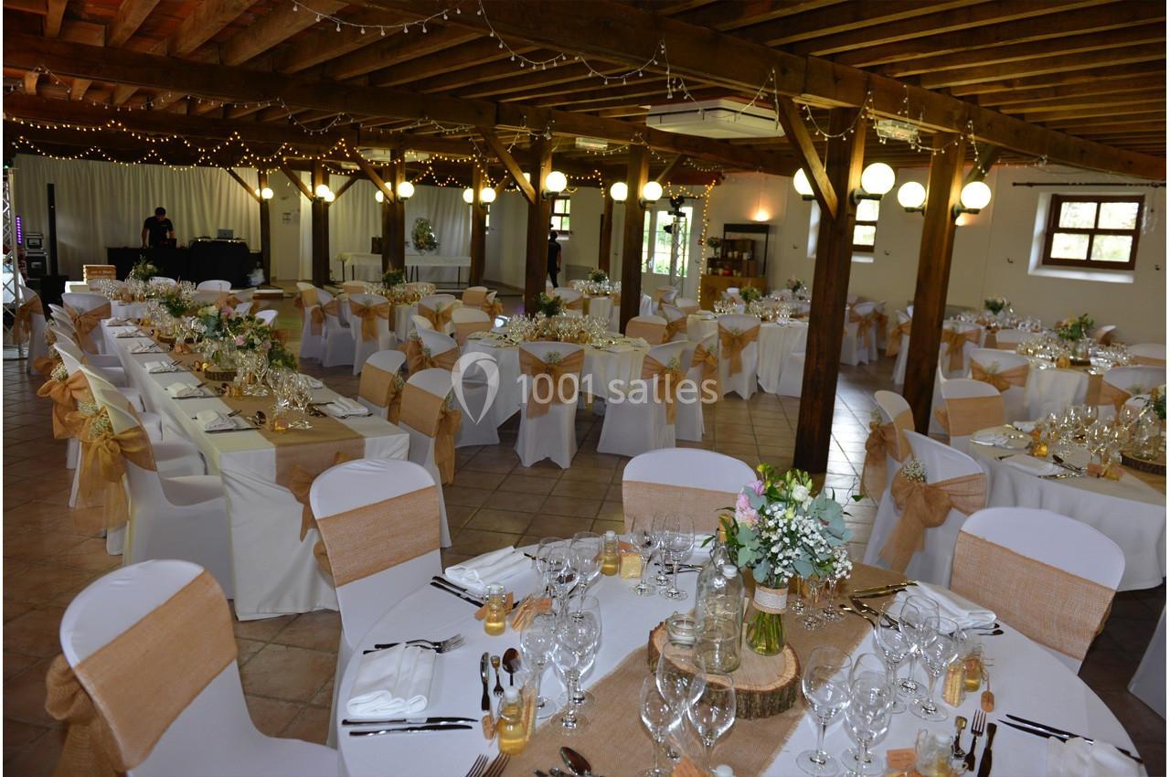Salle de réception décorée pour un mariage, avec tables dressées, chaises ornées de nœuds et guirlandes lumineuses…