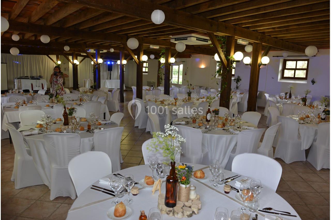 Salle de réception décorée avec des tables rondes dressées, nappes blanches et éclairage chaleureux.