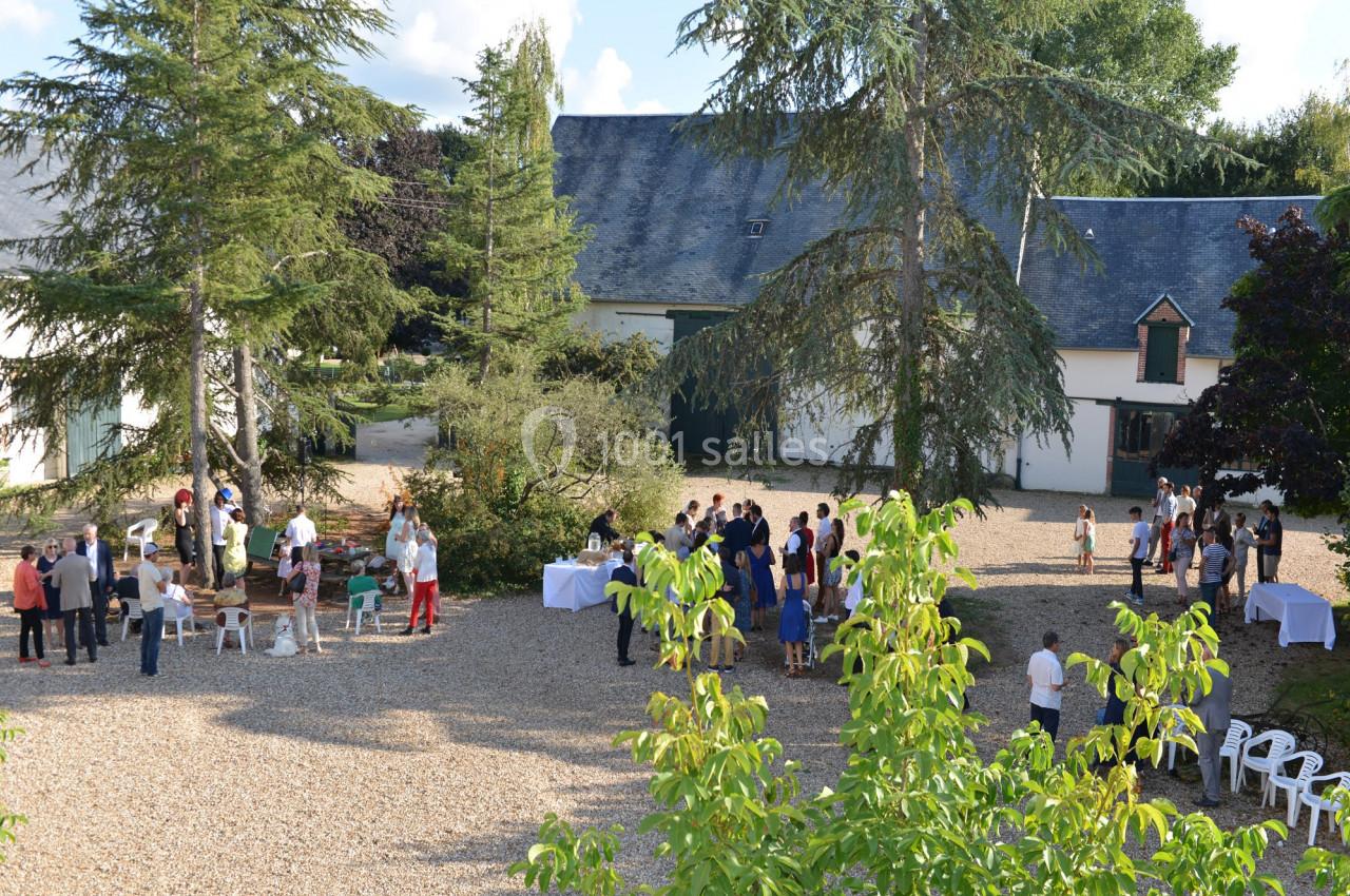 Groupe de personnes rassemblées dans une cour extérieure gravillonnée entourée de bâtiments et de végétation.