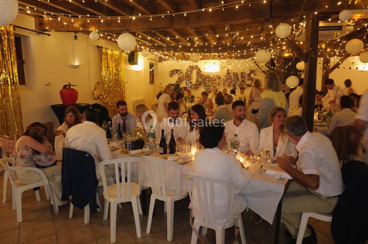 Salle décorée avec des guirlandes lumineuses et des invités assis à des tables lors d'une fête ou d'un événement.
