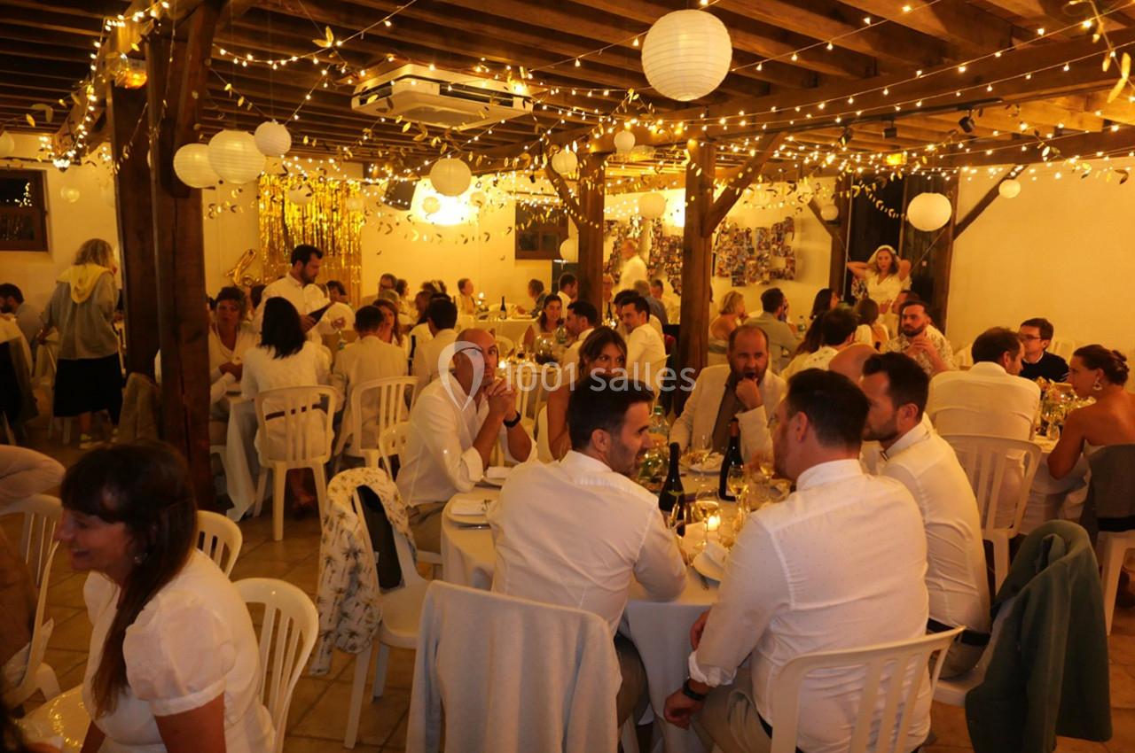 Des invités assis à des tables décorées de guirlandes lumineuses et de lanternes dans une salle de réception.