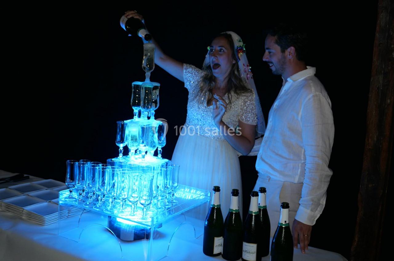 Une femme verse du champagne dans une fontaine lumineuse en verre, accompagnée d'un homme, dans un cadre festif.