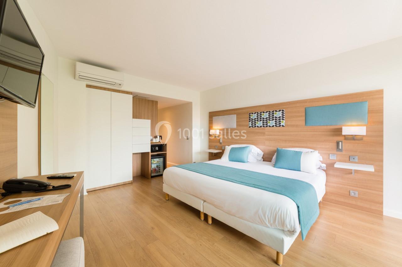 Chambre lumineuse avec lit double, décor moderne en bois clair, télévision murale et coin minibar.