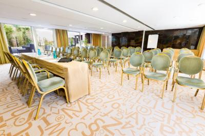 Chambre lumineuse avec lit double, fauteuils, table basse, valise et rideaux blancs laissant entrer la lumière naturelle.