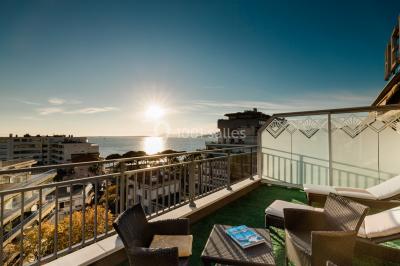 Chambre lumineuse avec lit double, fauteuils, table basse, valise et rideaux blancs laissant entrer la lumière naturelle.