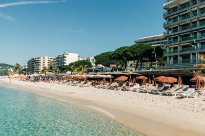 Chambre lumineuse avec lit double, fauteuils, table basse, valise et rideaux blancs laissant entrer la lumière naturelle.