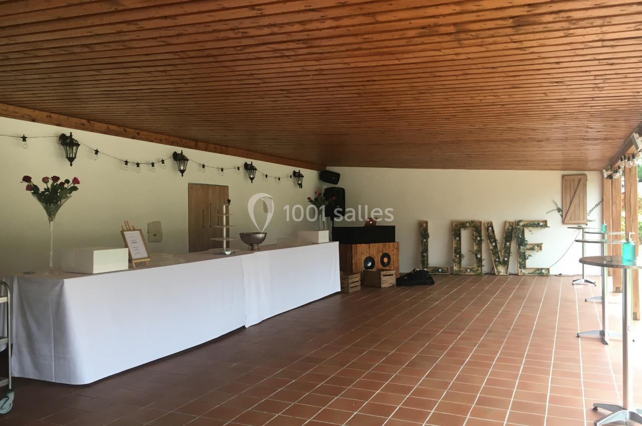 Salle avec plafond en bois, tables blanches alignées, décorations lumineuses et lettres ’LOVE’ en arrière-plan.