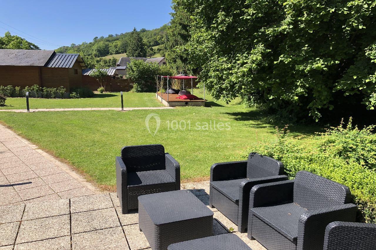 Mobilier de jardin en résine tressée sur une terrasse, avec pelouse, arbres et abri en bois en arrière-plan.