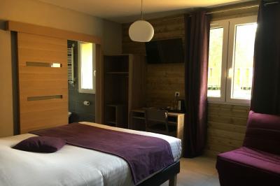 Chambre lumineuse avec lit double, bureau, télévision murale, fauteuil et fenêtre donnant sur l'extérieur.