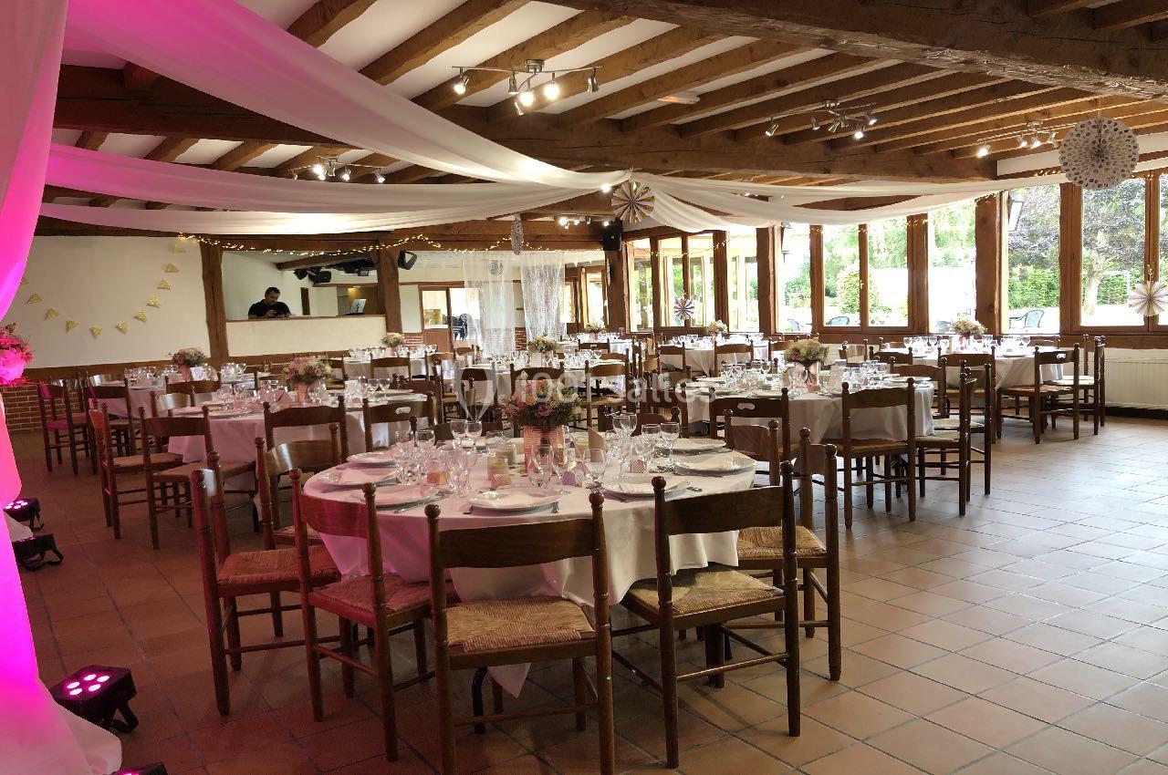Salle de réception décorée avec des tables rondes dressées, des nappes blanches et des guirlandes suspendues.