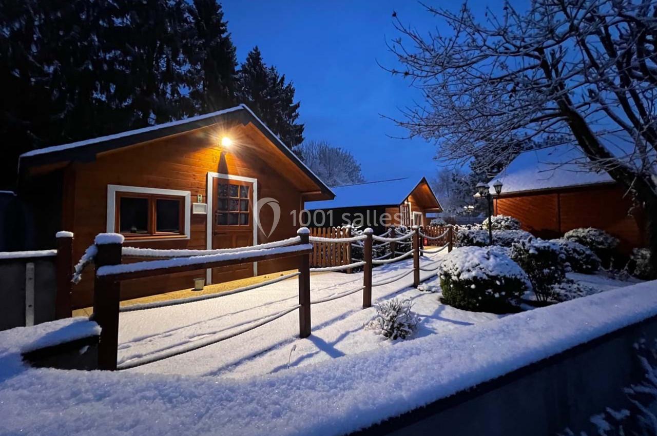 Chalets en bois éclairés par une lumière chaude, entourés de neige et d'arbres sous un ciel crépusculaire.