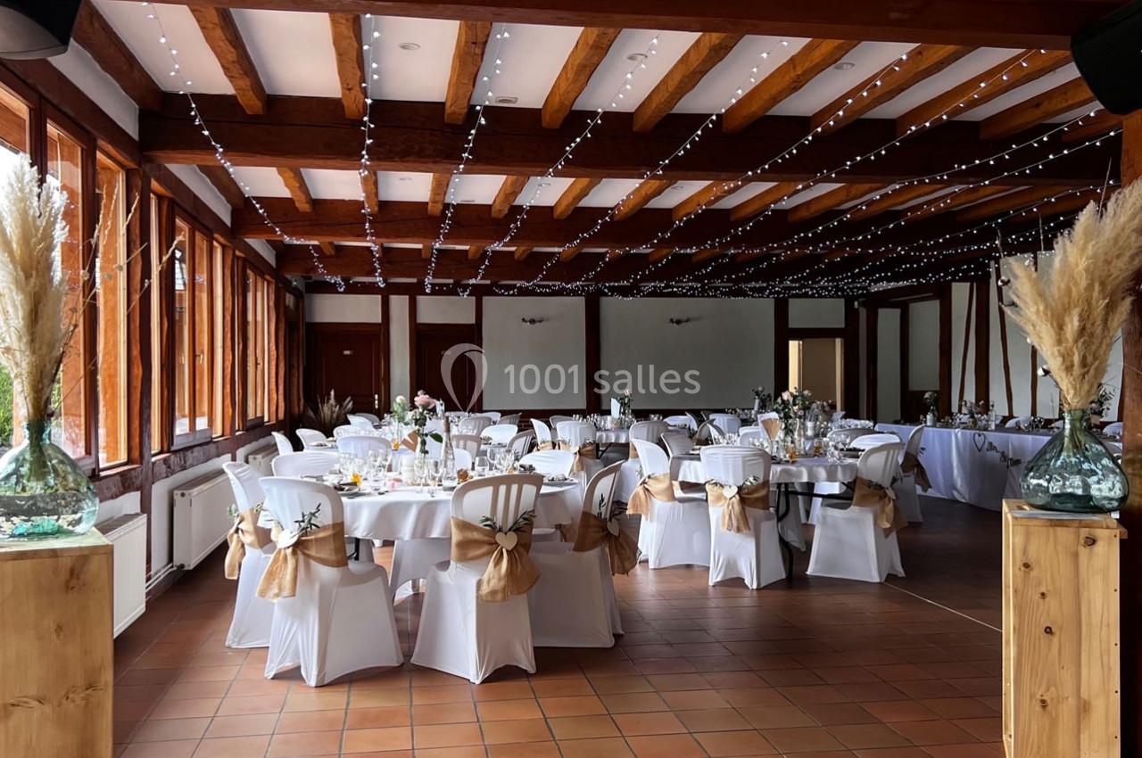 Salle de réception décorée avec des tables dressées, des chaises blanches ornées de nœuds et des guirlandes lumineuses au…