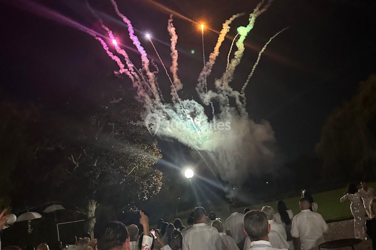 Un groupe de personnes en tenue blanche regarde un feu d'artifice illuminant le ciel nocturne.