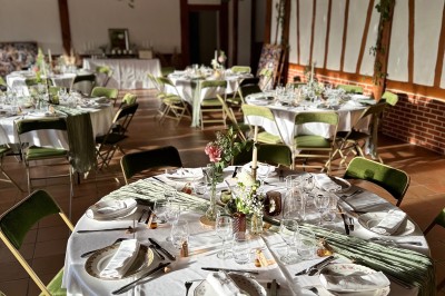Salle de réception décorée avec des tables rondes dressées, nappes blanches et chaises vertes, sous un plafond orné de…