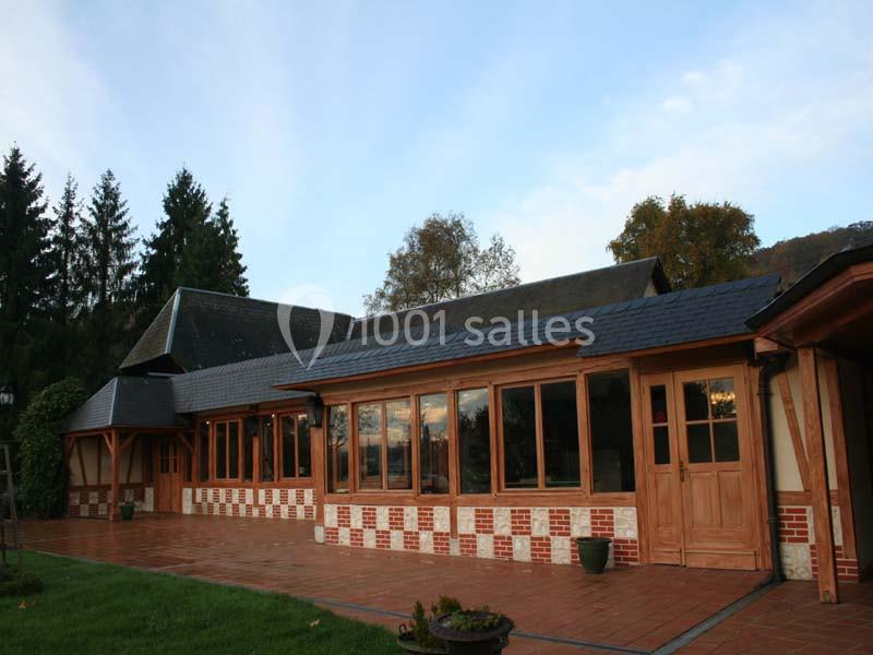 Maison à colombages avec façade en briques et bois, grandes fenêtres et terrasse en carrelage, entourée de verdure.
