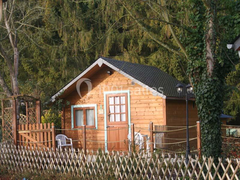 Petite cabane en bois avec toit sombre, entourée d'arbres et d'une clôture en bois, située dans un cadre naturel.