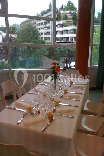 Table dressée avec nappes blanches, couverts alignés, verres, serviettes pliées et centre de table floral, près d'une baie…