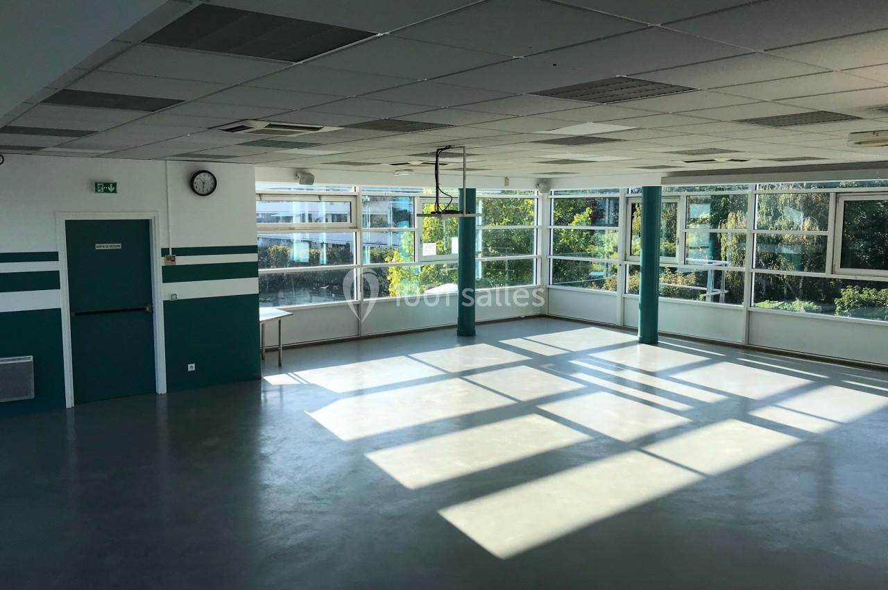 Salle lumineuse vide avec de grandes fenêtres laissant entrer la lumière naturelle, murs blancs et verts.