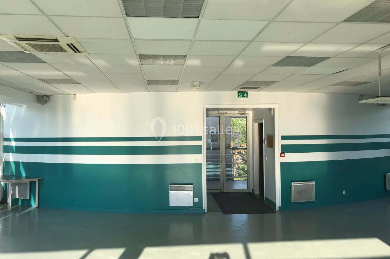 Salle lumineuse avec murs blancs et verts, plafond à dalles, porte vitrée au fond et lumière naturelle entrant par les…