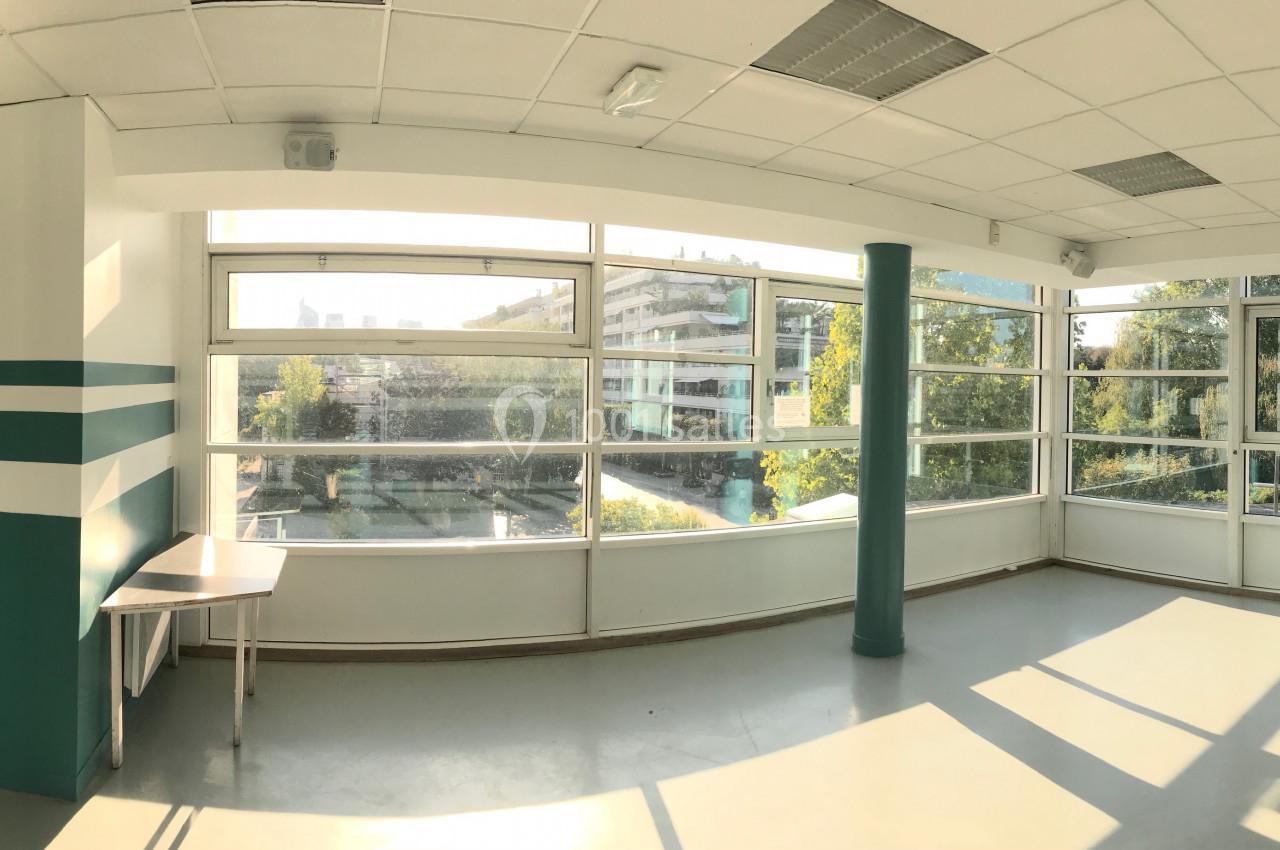 Vue panoramique d'une salle lumineuse avec de grandes baies vitrées donnant sur un espace extérieur arboré.