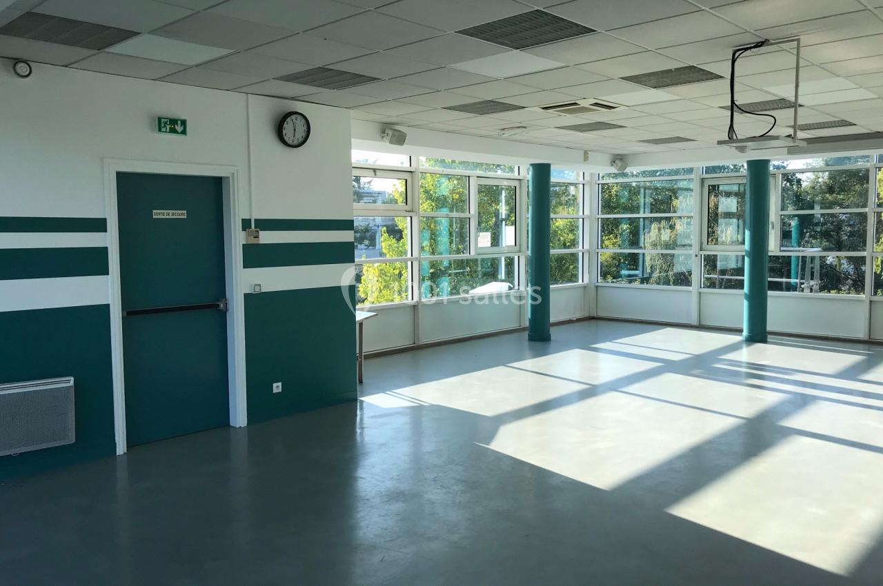 Salle lumineuse avec de grandes fenêtres, murs verts et blancs, sol en béton lisse et une porte fermée.