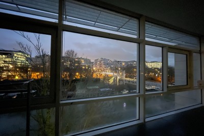 Vue nocturne depuis une fenêtre, montrant un parc éclairé, des arbres et des bâtiments en arrière-plan.