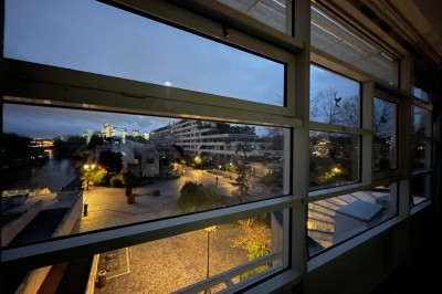 Vue nocturne depuis une fenêtre, montrant un parc éclairé, des arbres et des bâtiments en arrière-plan.