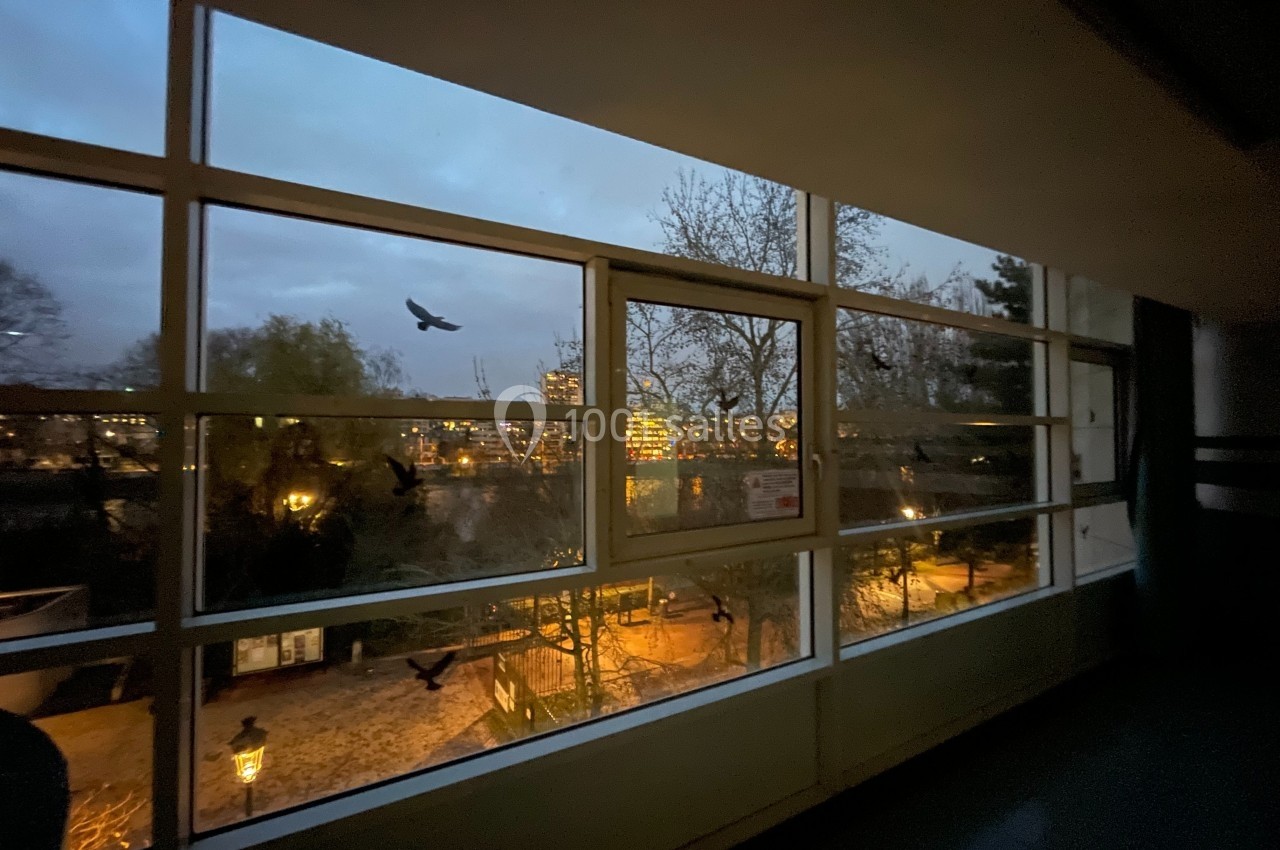 Vue nocturne depuis une fenêtre, montrant un parc éclairé, des arbres et des bâtiments en arrière-plan.